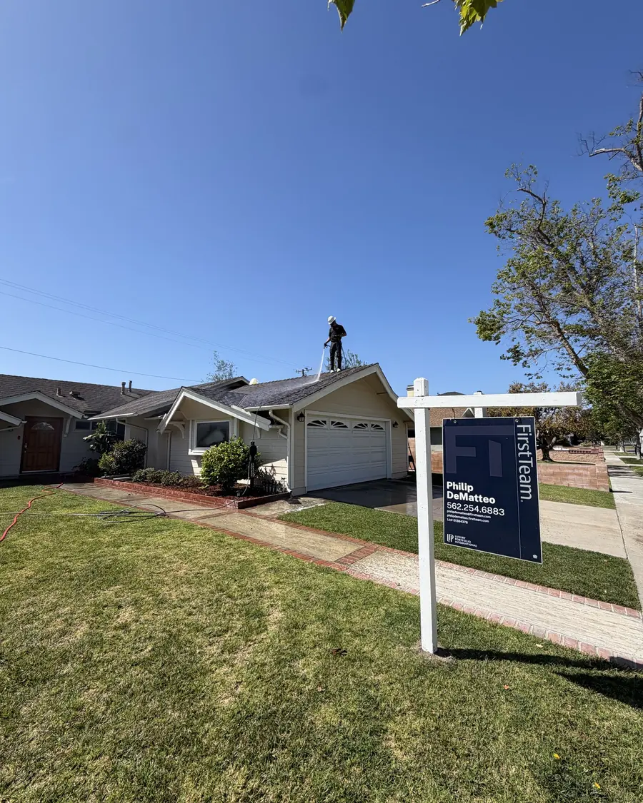 Titan crew member washing a roof with a for sale sign in the front yard