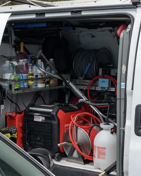 The side door of the Titan van open on shelves of cleaning chemicals, hose reels, a generator and a pump sprayer